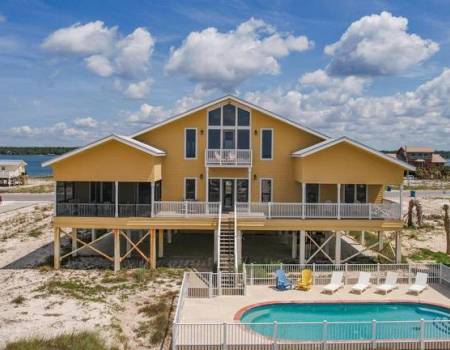 Yellow house on the beach with a fenced pool and lounge chairs